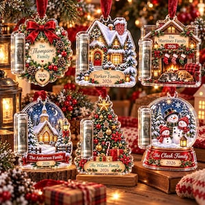 May include: Six clear acrylic Christmas ornaments featuring festive scenes including a wreath, a snowy house, a fireplace, a church, a decorated tree, and snowmen. Each ornament includes a rolled dollar bill and text for family names and 2026.
