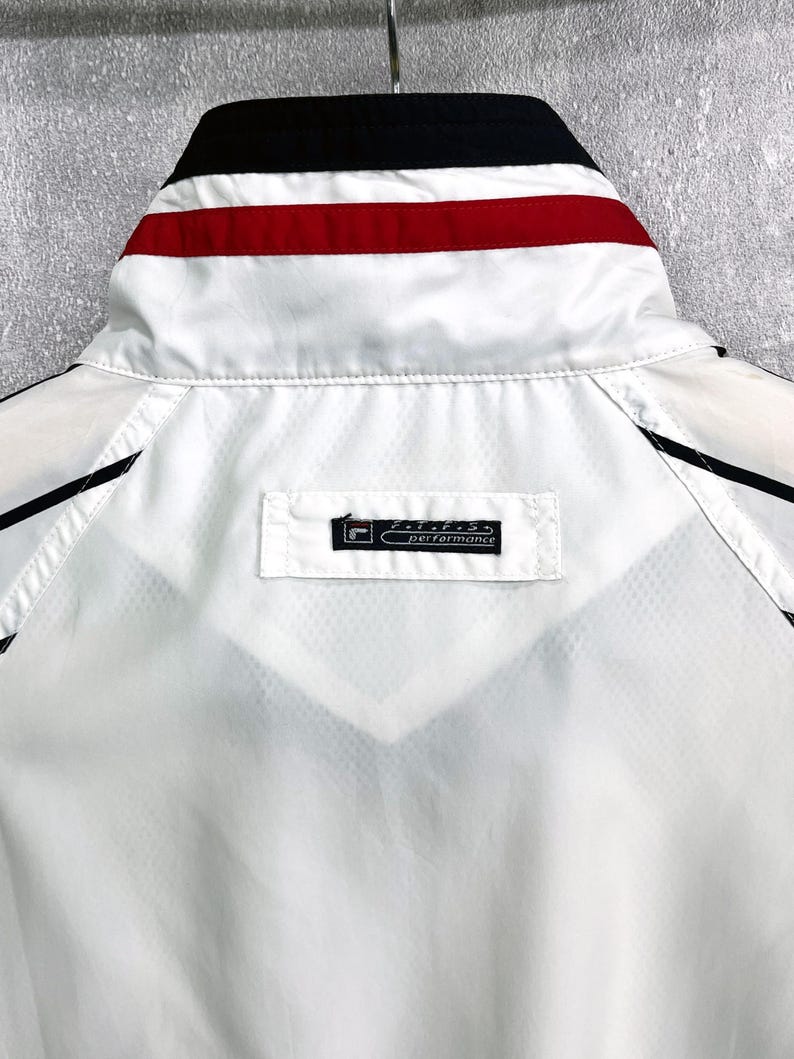 May include: White athletic jacket with black and red accents. The collar features black, red, and white stripes. The jacket has a small rectangular tag that reads "performance".