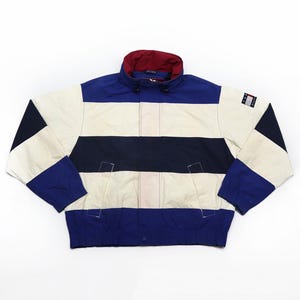 May include: A vintage jacket with a color block design. The jacket features a cream-colored body with navy and white horizontal stripes. The collar is navy blue with a red interior. The jacket has a small logo on the sleeve.