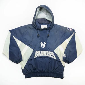 May include: A navy blue and white Yankees hooded pullover jacket. The jacket features the Yankees logo and team name in white. The design includes white and light gray accents on the sleeves and a drawstring hood. The jacket is made by Starter.