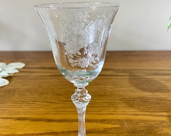 May include: A clear glass stemmed wine glass with a delicate floral etching design. The glass has a wide bowl and a long, slender stem.