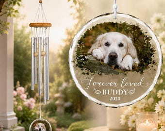 May include: A memorial wind chime featuring silver metal tubes and a circular glass ornament. The ornament displays a photograph of a golden retriever, the text "Forever loved", the name "BUDDY", and the year "2025" in white script lettering.