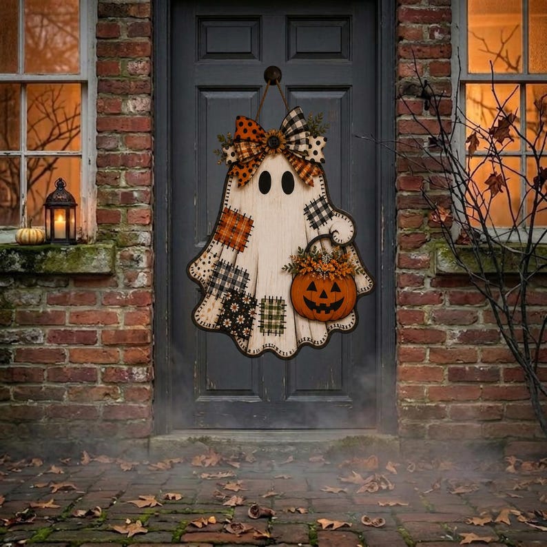 May include: A ghost-shaped wooden door hanger featuring a patchwork pattern of orange, black, and white plaid and floral fabrics. The ghost has two black oval eyes, a large decorative bow at the top, and holds a carved orange jack-o'-lantern.
