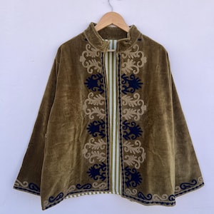 May include: Olive green velvet jacket with ornate embroidery in navy blue and tan. The jacket features a mandarin collar and a striped panel down the center. The jacket is hanging on a wooden hanger.