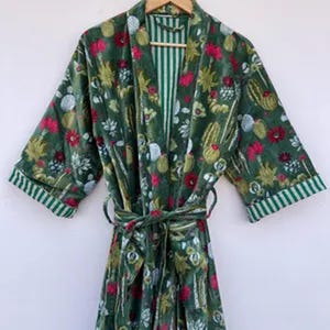 May include: Green floral print robe with a matching belt. The robe features a botanical pattern with red and white flowers, green cacti, and other foliage. The sleeves and inner lining have green and white stripes.