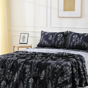 May include: A bed with a dark blue floral patterned comforter and matching pillowcases. The bed is made up with a white sheet. A small side table with a lamp is next to the bed.