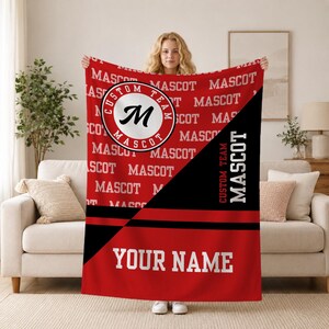 May include: A red and black fleece blanket featuring a repeating pattern of the text MASCOT, a circular logo with the letter M and the text CUSTOM TEAM MASCOT, a diagonal black stripe, and the text YOUR NAME printed in white block letters.