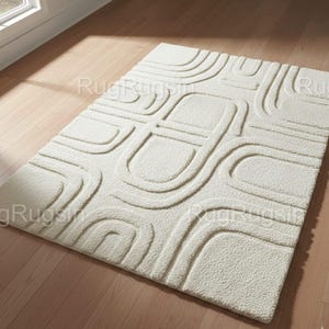 Pode incluir: Tapete retangular creme com um padrão geométrico em relevo. O design apresenta linhas curvas e formas retangulares, criando uma superfície texturizada. O tapete é colocado sobre um chão de madeira clara. Um toque suave e neutro para qualquer ambiente.