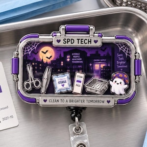 May include: A rectangular badge reel with a purple and silver frame featuring a spooky night scene with a full moon, bats, and a ghost. The text reads SPD TECH and CLEAN TO A BRIGHTER TOMORROW. It includes miniature medical instrument charms.