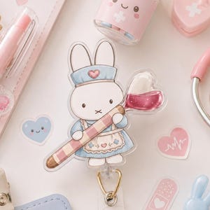 May include: A selection of pastel-coloured medical-themed stationery and accessories. Includes a nurse bunny badge reel, a pink stethoscope, a pill bottle, a notepad, a pen, and heart-shaped stickers. The badge reel features the text "NURSE".