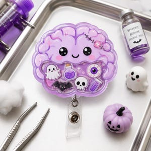 Può includere: Un portabadge a forma di cervello viola con un volto sorridente, una cicatrice cucita e una finestra trasparente riempita di ciondoli in miniatura galleggianti, tra cui un fantasma, un pipistrello, un teschio, un bulbo oculare e boccette.