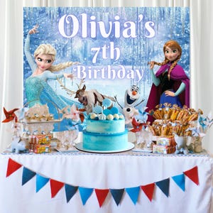 Puede incluir: Una decoraci&oacute;n de cumplea&ntilde;os con un pastel azul de dos pisos, un fondo con Elsa, Anna, Sven y Olaf, y el texto Olivia's 7th Birthday. La mesa est&aacute; decorada con una guirnalda de banderines rojos y azules y varios dulces de fiesta.