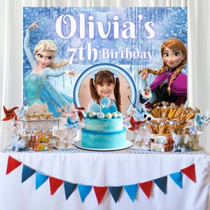 Puede incluir: Un tel&oacute;n de fondo para fiestas con Elsa y Anna de Frozen, el texto Olivia's 7th Birthday, un marco de fotos circular central, un pastel azul de dos niveles y una mesa decorada con banderines rojos y azules y diversos dulces festivos.