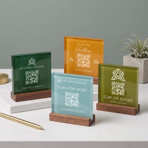 May include: Four square acrylic signs in green, orange, light blue, and olive green, each featuring a white QR code, the Aeterna Designs logo, and text including Scan to Connect, Scan to Follow, Scan for More, and Scan for Reviews, set on wooden bases.