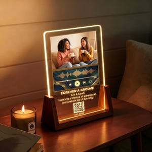 May include: A rectangular acrylic plaque with an LED light border, set in a dark wood base. It displays a photo of two people, a sound wave graphic, and the text: FOREVER A GROOVE, Lily & Sarah, Here's to a lifetime of adventures and a whole lot of dancing!, a QR code, and Est. 2024.