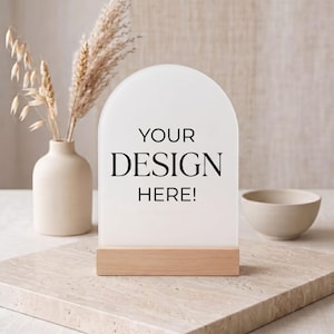 May include: An arched, frosted acrylic sign with a light wood base. The sign features the black printed text "YOUR DESIGN HERE!" centered on the front surface. The piece is designed for custom signage and display purposes in a neutral setting.