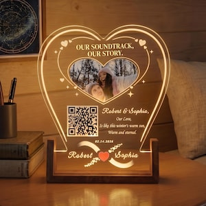 Op de afbeelding: Een hartvormig acryl lichtdisplay met een centrale foto van twee personen, een QR-code en de tekst "OUR SOUNDTRACK, OUR STORY." en "Robert & Sophia, Our Love, Is like this winter's warm sun, Warm and eternal." met de datum 14-02-2026.