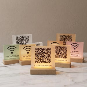 May include: A collection of illuminated square acrylic signs with wooden bases, each featuring printed QR codes, Wi-Fi symbols, and network credentials including TheCraftHouse, GlassNet61, ETSY.HeartlineCraft, and PubHub Access with password accessfree@2026.