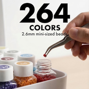 May include: A close-up of a craft set with 264 colors of 2.6mm mini-sized beads. A hand holds tweezers with a single red bead. The beads are in small, clear bottles with colored lids. The text "264 COLORS" is at the top.