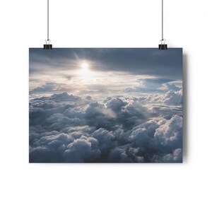 Könnte beinhalten: Ein Poster-Druck mit einer Fotografie eines bewölkten Himmels mit Sonnenschein. Die Wolken sind weiß und grau, und die Sonne ist hell und gelb. Das Poster wird von zwei schwarzen Clips gehalten.