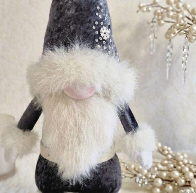 May include: A plush gnome doll with a dark gray body, arms, and hat. The hat is decorated with sequins and a snowflake. It has a large white fluffy beard, pink nose, and white fur cuffs. A decorative item for the holiday season.