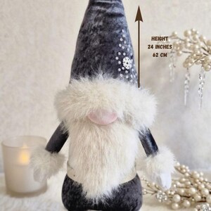 May include: A plush gnome doll with a gray velvet hat and a white faux fur beard and trim. The gnome is 24 inches (62 cm) tall and has a pink nose and white boots. The hat is decorated with sequins.
