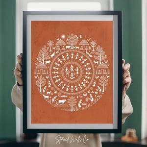 May include: Framed art print featuring a circular design with white figures and elements on an orange background. The artwork depicts a village scene with people, animals, houses, and trees. The text "Storied Walls Co" is at the bottom.