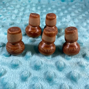 Op de afbeelding: Zes kleine, bruine, keramische potten met een lichtbruine bovenkant en een bruin en wit patroon. De potten zijn in een halve cirkel op een lichtblauw oppervlak gerangschikt.