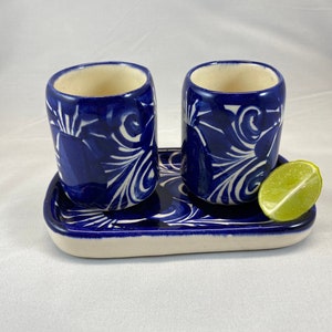 Puede incluir: Dos vasos de chupito de cerámica azul y blanca con un diseño floral, sentados en una bandeja a juego con una rodaja de lima.