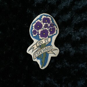 May include: A white fabric patch with a bouquet of purple flowers and a banner that reads "Yo Te Esperaré".