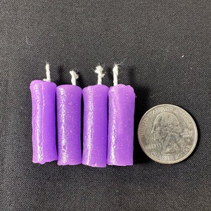 May include: Four purple taper candles with white wicks. The candles are about the size of a US quarter.