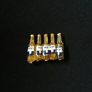 May include: Six miniature glass bottles of Corona Extra beer. The bottles are clear and contain a yellow liquid. The bottles are labelled with the Corona Extra logo and text.