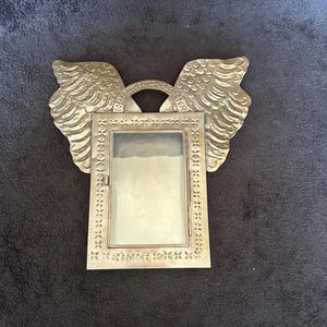 Peut inclure: Un cadre photo en métal argenté avec des ailes d'ange. Le cadre est de forme rectangulaire avec un insert en verre et une bordure décorative. Les ailes présentent des motifs de plumes détaillés.