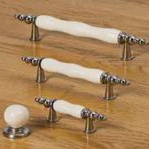 May include: Three cabinet pulls and one round cabinet knob. Each piece features a smooth, off-white ceramic center handle or body with polished silver-toned metal hardware at the ends, showcasing a tiered, decorative design on the metal mounts.