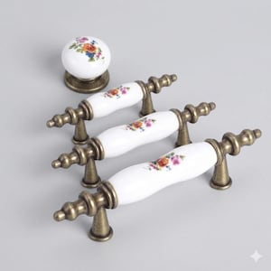 May include: A collection of white ceramic cabinet handles and a matching knob. The handles feature floral patterns and antique brass-coloured metal hardware. The knob is round with a floral design. Suitable for kitchen or bathroom cabinets.