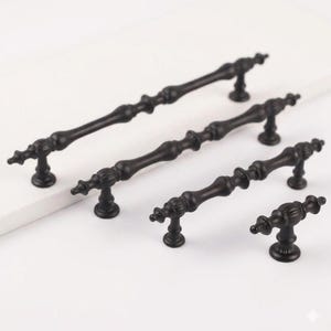 以下が含まれることがあります： 装飾的でヴィンテージなデザインの、黒いキャビネットプル4個セット。プルはサイズが異なり、中央のバーと装飾的な端があります。ハードウェアは金属製で、引き出しやキャビネットに適しています。