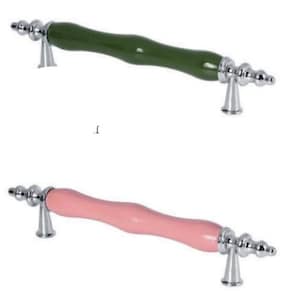Può includere: Due maniglie per mobili. Una ha una maniglia verde curva con dettagli argentati. L'altra ha una maniglia rosa curva con dettagli argentati. Entrambe hanno un design decorativo e ornato.