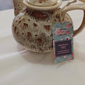 May include: A vintage brown and cream-coloured teapot with a lid and handle. The teapot has a speckled design and a tag that reads "Allen Harvey Teapot."