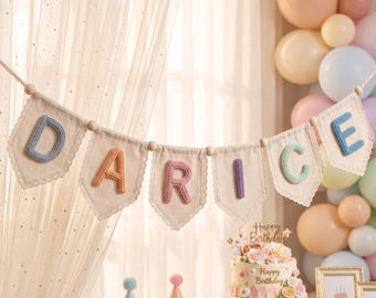 May include: A decorative banner featuring off-white fabric pennants with scalloped lace edges, strung together with wooden beads. Each pennant displays a single, three-dimensional, pastel-colored crocheted letter spelling out the name DARICE.