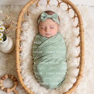 K&ouml;nnte beinhalten: Ein Neugeborenes, eingewickelt in eine salbeigr&uuml;ne Puckdecke mit dem in verschiedenen wei&szlig;en Schriftarten aufgedruckten Namen James Taylor. Das Baby tr&auml;gt ein passendes salbeigr&uuml;nes Schleifen-Stirnband. Das Kind liegt in einem Rattankorb.
