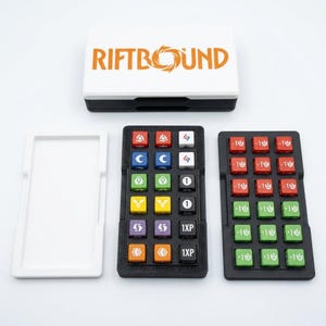 May include: A board game set with the text "RIFTBOUND" in orange on a white and black box. The set includes two black game boards with colorful square tokens and a white tray.