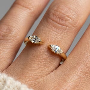 Op de afbeelding: Een open gouden ring met twee heldere marquise-geslepen stenen aan de uiteinden. De band is van gepolijst goud en de stenen zijn horizontaal gezet. De tekst ELARIS JEWELS WHERE ELEGANCE SHINES is zichtbaar in de linkerbovenhoek van de afbeelding.
