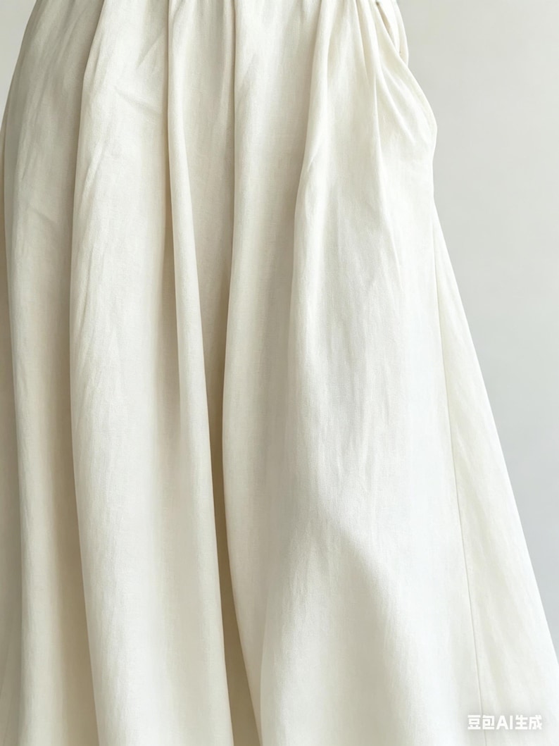 May include: Close-up of a cream-colored fabric with soft folds and a flowing drape. The fabric appears to be a lightweight material, possibly linen or cotton, with a subtle texture. The image highlights the fabric's natural color and the way it catches the light.