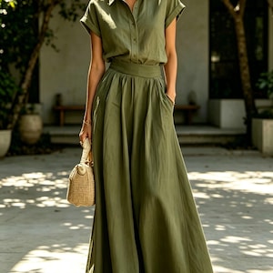 May include: An olive green two-piece outfit consisting of a short-sleeved button-down shirt and a floor-length skirt. The outfit is paired with a woven handbag. The model is wearing sunglasses and sandals.