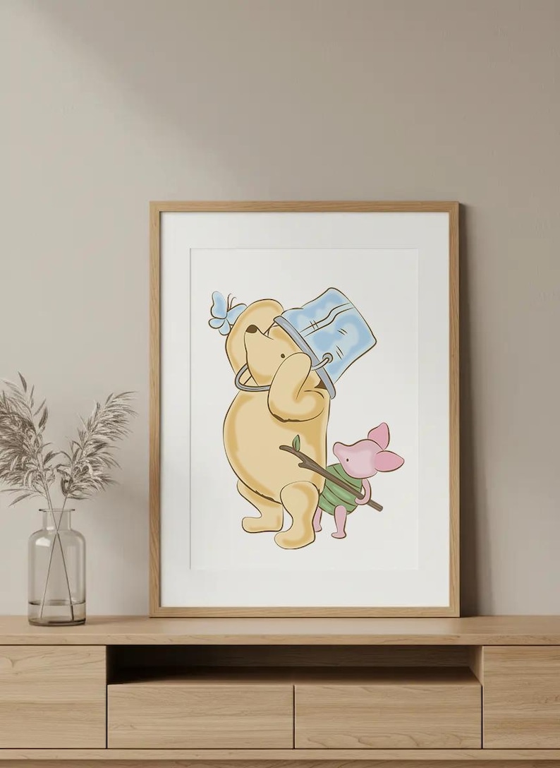 May include: A framed print featuring a cartoon illustration of Winnie the Pooh and Piglet. Pooh is holding a blue bucket, and Piglet is carrying a stick. The artwork has a soft color palette and is displayed on a wooden surface.