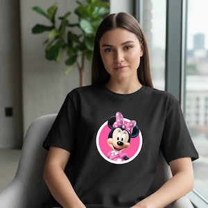 Puede incluir: Camiseta negra con un dise&ntilde;o de Minnie Mouse. El gr&aacute;fico muestra a Minnie Mouse con un lazo y un vestido de lunares rosas, dentro de un c&iacute;rculo rosa. La camiseta la lleva una persona.