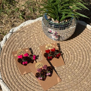 May include: Three pairs of heart-shaped earrings on brown cardboard display cards. Each pair features a leopard print heart, a solid coloured heart top, and small dangling cherry charms. The colours include bright pink, deep red, and light pink.