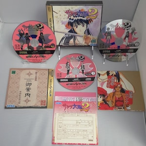 May include: A Sega Saturn Sakura Wars 2 video game set including a game case, three discs labeled Disc 1, Disc 2, and Disc 3, a printed manual, a promotional flyer, and a registration card. The items feature anime-style character illustrations.
