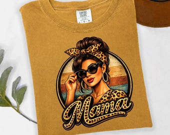May include: Mustard-colored t-shirt featuring a graphic of a woman wearing sunglasses and a leopard print headband. The word "Mama" is written in a leopard print font. The shirt is made of a soft, comfortable material.