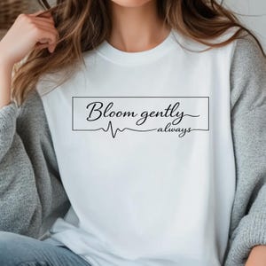 May include: A white ceramic mug with a black handle and the text "But First, Coffee" in a bold, black font. The mug is set against a neutral background, highlighting its simple design.